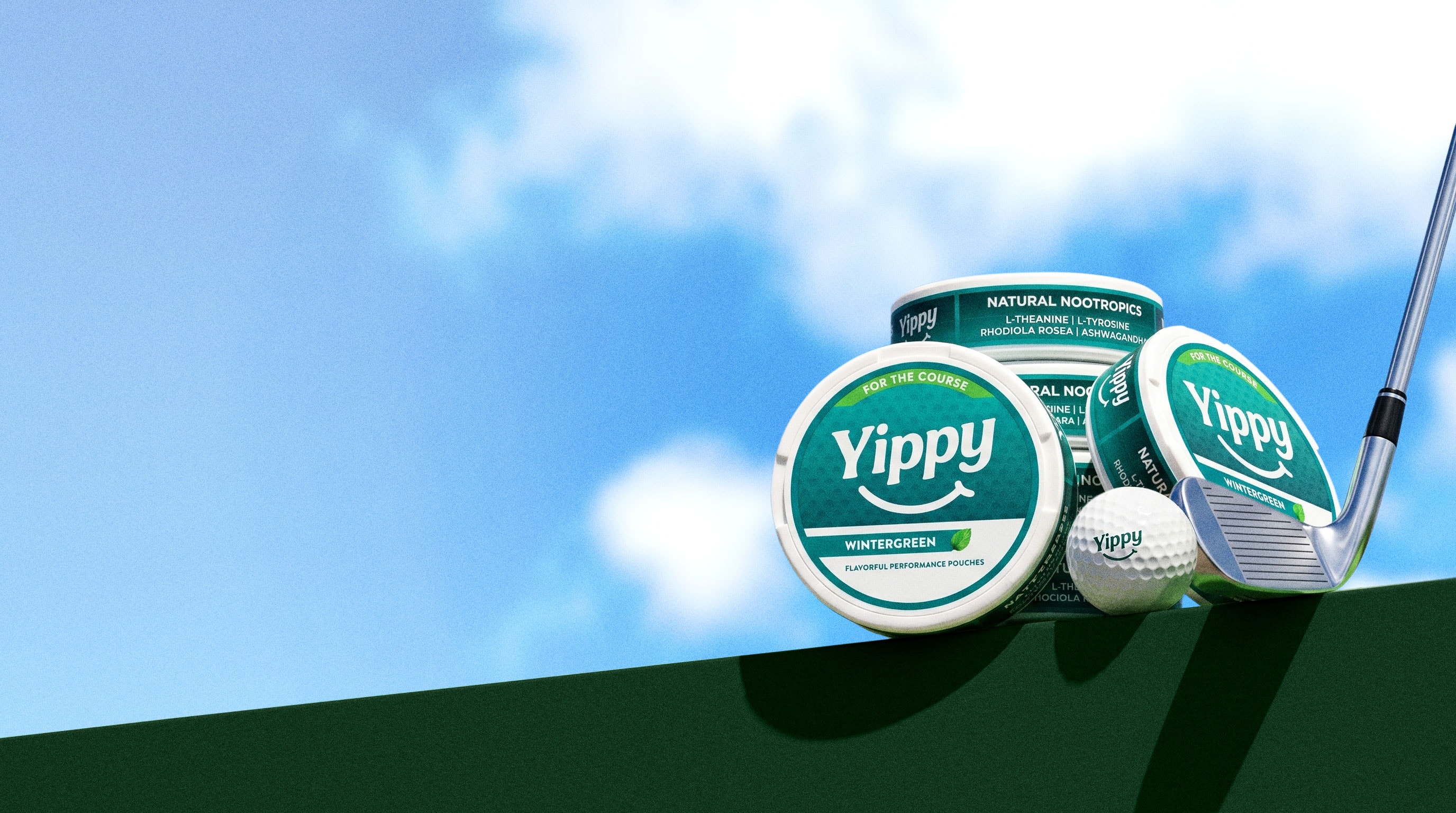 Still life of Yippy For The Course Wintergreen tins on a green putting surface with a golf ball and putter under a blue sky with drifting clouds