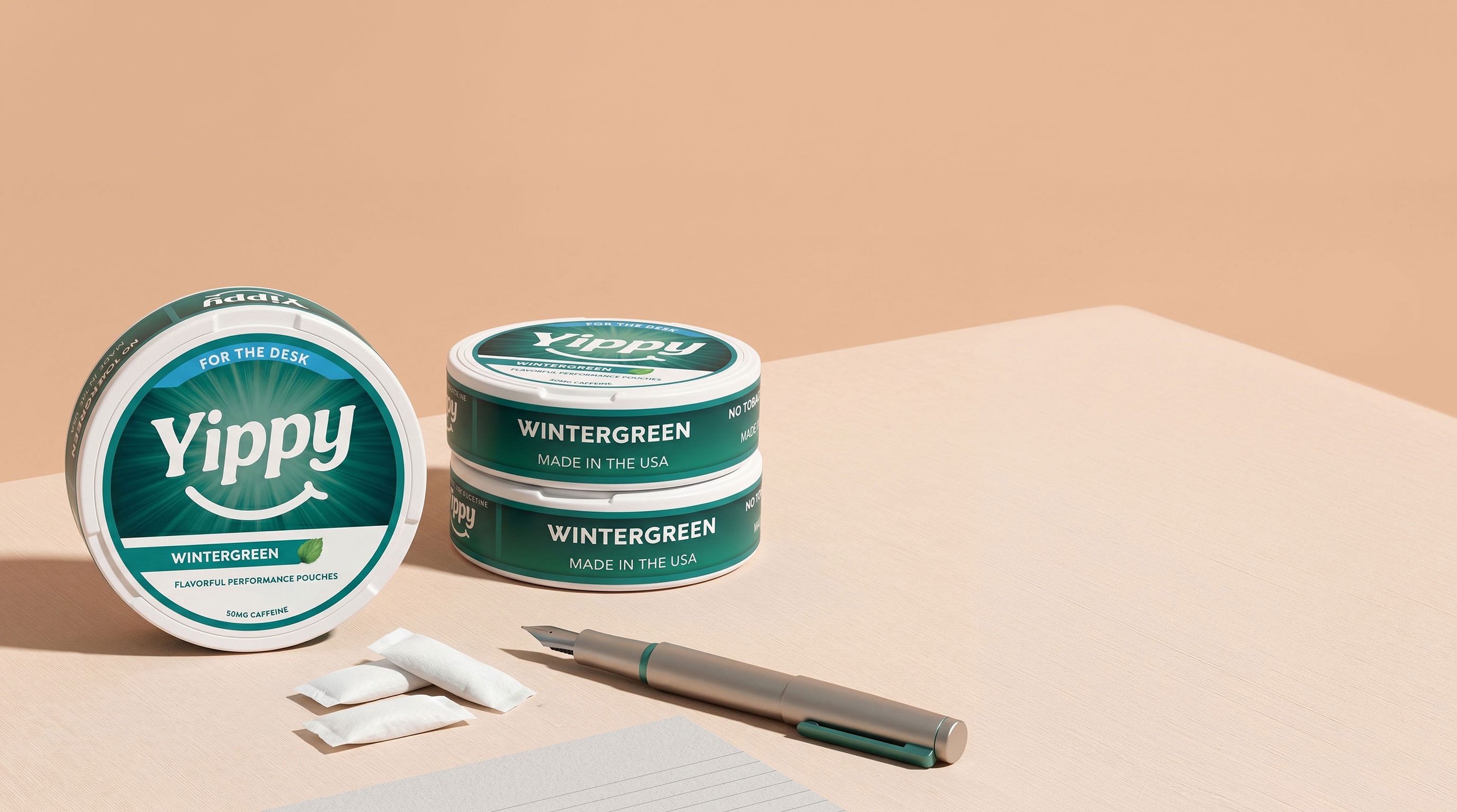 Still life of Yippy For The Desk Wintergreen tins arranged with a fountain pen, paper, and pouch packets on a peach paper backdrop