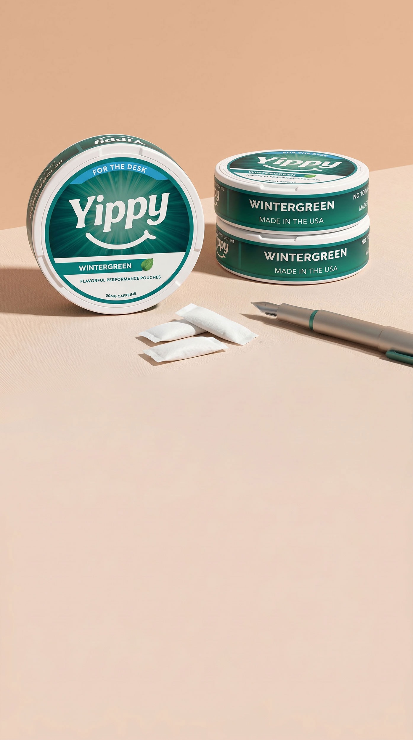 Still life of Yippy For The Desk Wintergreen tins arranged with a fountain pen, paper, and pouch packets on a peach paper backdrop