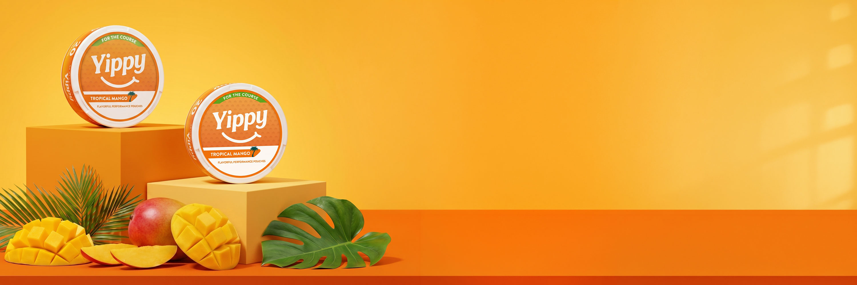 Yippy Tropical Mango pouches on orange podiums with fresh mango, peach, and monstera leaves in a sunlit tropical studio set